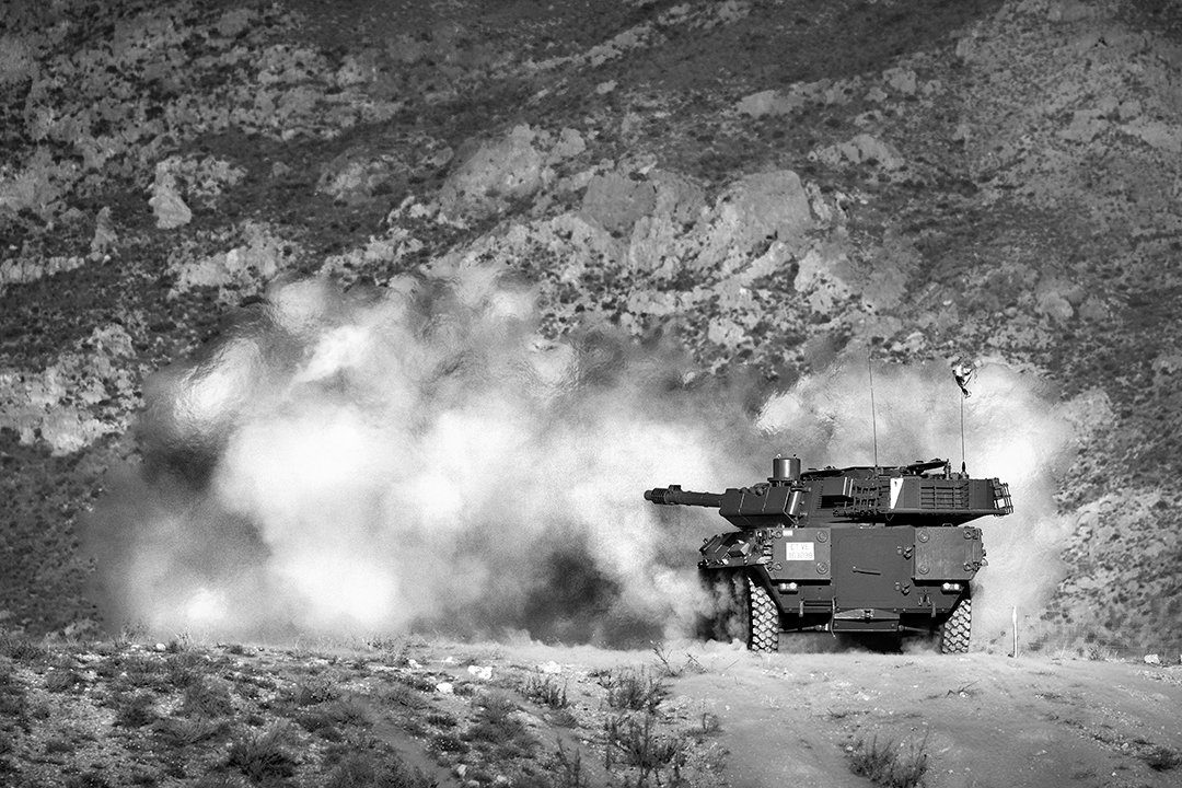 A military vehicle moving through dust and vegetation.